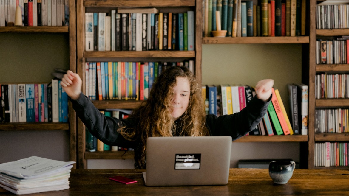 girl sat at desk with laptop in front of her waving her arms